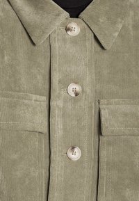 Olive green corduroy shirt jacket with a pointed collar, two front pockets, and three button closures. Textured fabric with vertical ribbing.