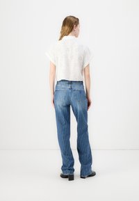 Blouse blanche à manches courtes avec des détails en dentelle, associée à un jean en denim bleu à pattes d'éléphant avec des rayures blanches verticales et une taille haute.
