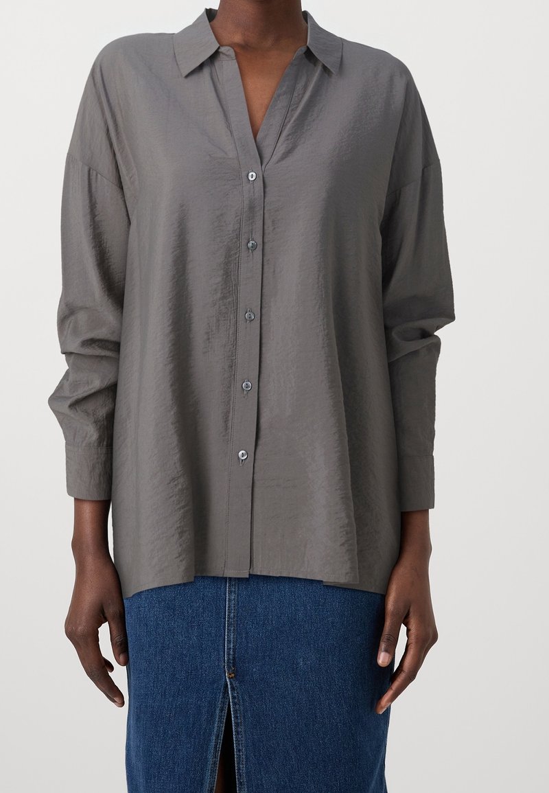 Chemise grise à boutons avec col, manches longues et tissu texturé. Présente une coupe légèrement décontractée, avec des boutons sur le devant et des poignets.