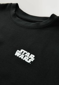 Hanorac negru, confecționat dintr-un material moale, având un logo alb "STAR WARS" expus proeminent pe față. Design cu guler rotund.