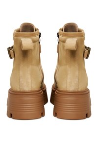 Tan nubuck enkelboots met een stevige bruine rubberen zool, voorzien van zijritsen en een gespdetail aan elke buitenzijde.