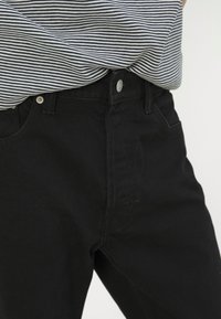 Personne portant un jean noir taille haute et un chemisier rayé noir et blanc rentré à la taille.