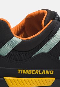 Sneaker nera con accenti verde menta, foderatura arancione e materiale nero testurizzato. Presenta un logo giallo prominente "TIMBERLAND" sul lato.