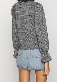 Blusa a scacchi bianca e nera con maniche a sbuffo e schiena con taglio a chiave, abbinata a una mini gonna in denim azzurro chiaro con orlo frangiato e tasche.