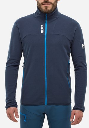 Veste en polaire bleu marine pour homme avec un col haut, une fermeture éclair bleue contrastante et des poches latérales zippées. Présente le logo de la marque sur la manche gauche.