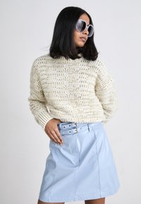 Pullover in crema lavorato a maglia con motivo testurizzato, abbinato a una gonna in pelle azzurro chiaro con doppia fibbia. Modella che indossa occhiali da sole oversize.