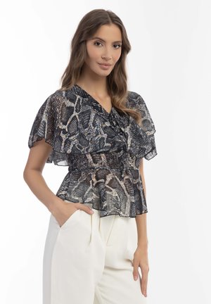 Durchsichtige Bluse mit schwarz-creamfarbenem Schlangendruck, mit Flatterärmeln, V-Ausschnitt, gerafftem Taillenteil und Peplum-Design, kombiniert mit weißen, plissierten Hosen.