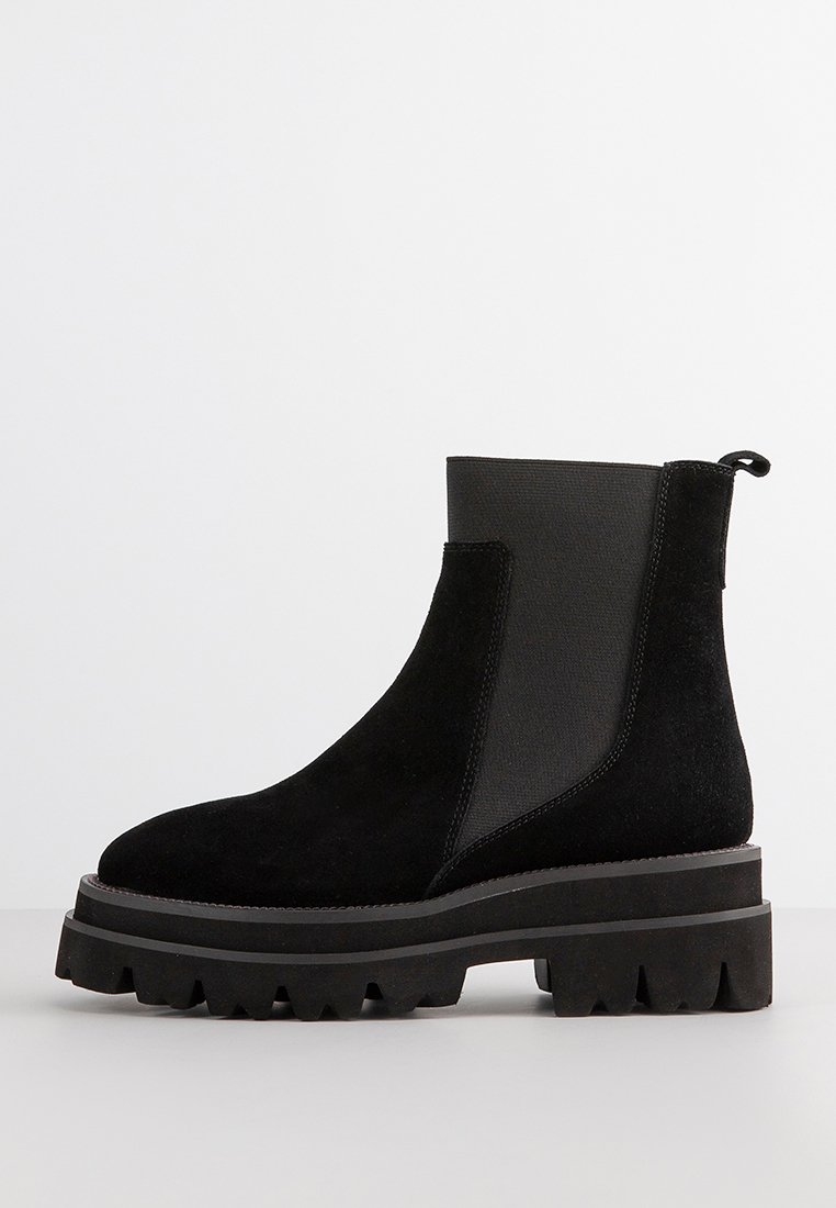 Black suede ankle boot with elastic panels, chunky black rubber sole, and pull tab at the back. Features smooth and textured areas.