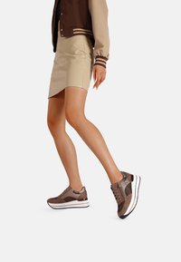 Scarpe da ginnastica marroni realizzate con un mix di materiali lisci e testurizzati, con una spessa intersuola bianca e una suola scura, abbinate a una gonna beige.