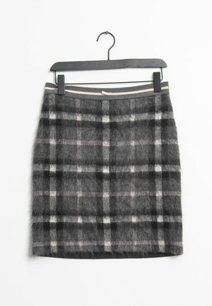 Jupe en lainage gris et noir à carreaux avec des lignes blanches et rose clair, suspendue à un cintre noir sur un fond blanc.