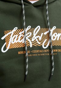 Grøn hættetrøje med snore, prydet med hvid og orange tekst. Teksten inkluderer "Jack & Jones," sat mod en stribet orange baggrund.