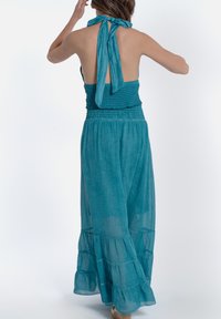 Jumpsuit teal, senza maniche, con scollo all'americana, corpino arricciato, gambe ampie e orlo a strati. Tessuto morbido e leggero.