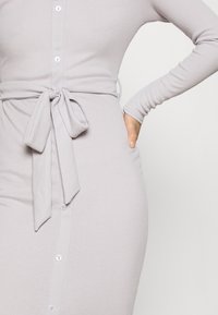 Hellgraues, geripptes Kleid mit tailliertem Schnitt, langen Ärmeln, Knopfleiste vorne und gebundenem Taillengürtel. Verfügt über sichtbare Knöpfe und Taschen.