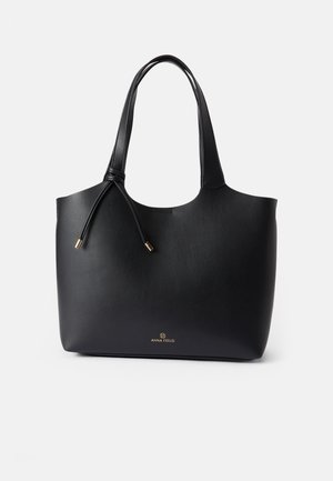 Sac fourre-tout en cuir noir avec une texture lisse, ouverture sur le dessus, deux poignées, et un logo doré subtil à la base. Caractérisé par une fermeture à cordon.