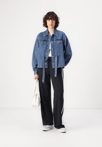 Veste en denim avec de grandes poches avant, un fermoir à boutons, une taille cintrée et des manches larges. Associée à un pantalon de survêtement noir et des baskets blanches.
