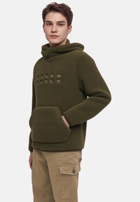 Olivroheline fliisist kapuutsiga, ees tasku ja embossed brändi logo. Pehme tekstuur, laiem lõige ja regulaarne pikkus.