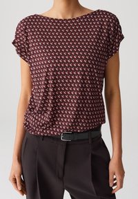 Bordeaux kortærmet bluse med et geometrisk mønster af små hvide trekanter. Blødt stof, afslappet pasform, med rund halsudskæring og oprullede ærmer.