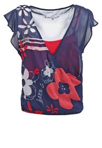 Mörkblå blommig topp med V-hals och flygande ärmar. Har röda och vita blommönster, över ett enfärgat röd underlager. Genomskinlig textur.