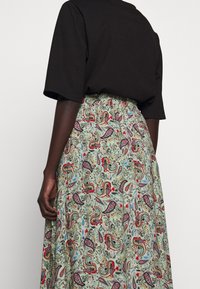 Černé tričko s krátkým rukávem v kombinaci se zelenou sukní s paisley vzorem a elastickým pasem. Má červené a modré květinové akcenty.