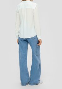 Camicia bianca a maniche lunghe con piega sul retro, abbinata a pantaloni cargo ampi blu chiaro con tasche laterali e una vestibilità comoda.