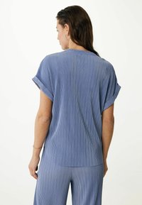 Top de manga corta a rayas azules con puños enrollados y un ajuste relajado, fabricado en un tejido ligero. Textura suave y un brillo sutil.