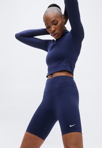 Crop top athlétique bleu marine et shorts taille haute en tissu extensible, avec un petit logo Nike blanc sur les shorts.