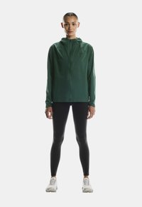 Roheline, lukuga jope kapuutsiga, valmistatud siledast kangast. Mustade retuuside ja heledate tossudega on sportlik välimus täielik.