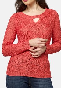 Koralowy sweter dziergany z teksturowanym wzorem, okrągłym dekoltem z wycięciem oraz długimi rękawami. Dół swetra jest ściągany ściągaczem dla lepszego dopasowania.