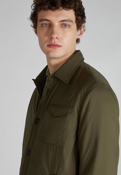 Chaqueta ligera verde olivo con cierre de botones, gran bolsillo en el pecho y cuello clásico. Textura suave y ajuste entallado.