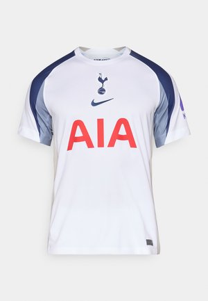 Hvit fotballtrøye med blå og grå detaljer, med en stor rød "AIA" logo på forsiden og en klubbemblem på brystet. Laget av lett stoff.