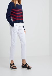Navy sweater with red stripes, white layered shirt underneath, paired with white trousers and black platform sandals with white soles and straps.