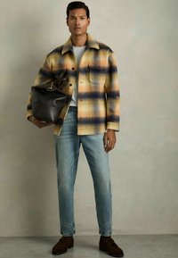 Chaqueta de mezcla de lana a cuadros amarillos y azules, camiseta blanca, jeans de mezclilla azul claros, zapatos de cuero marrón, llevando un bolso de cuero marrón.