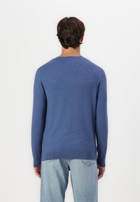 Blue long-sleeve sweater with a round neckline, soft texture, and ribbed cuffs. Worn with light blue jeans, displayed from the back.