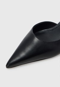 Musta nahkainen teräväkärkinen kenkä, jossa on sileä pinta, avoimet sivut ja hoikka siluetti. Sisäpuoli on myös musta ja siinä on siistit linjat.