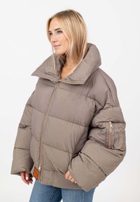 Giacca taupe con effetto imbottito, colletto oversize, chiusura con zip e orlo a coste. Presenta una tasca laterale con dettaglio a zip. Finitura liscia e opaca.