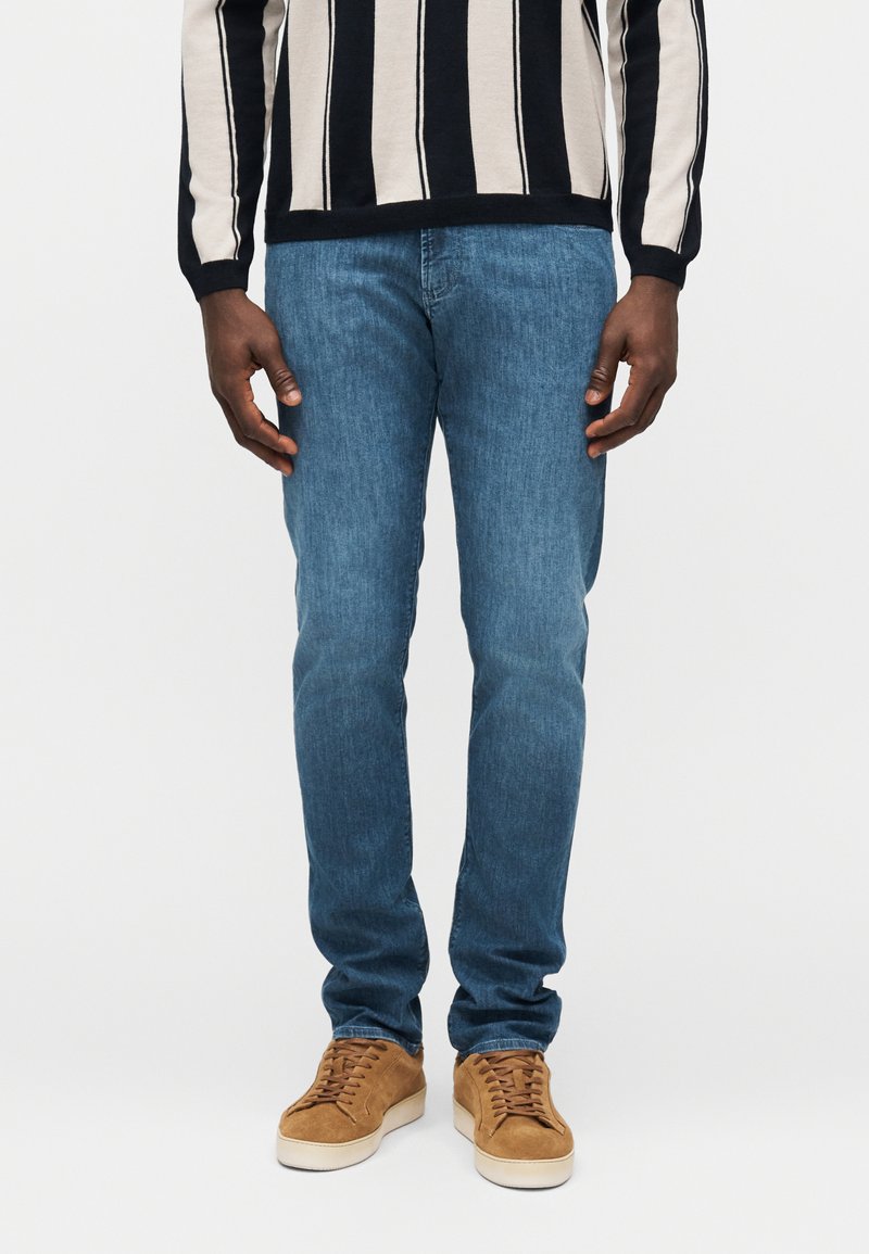 Svetlo modre kavbojke iz jeansa, s kratkim krojem in minimalnim bledenjem, kombinirane z rjavimi semišnimi supergami in črtasto majico.