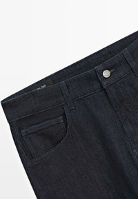 Jeans in denim blu scuro con un fit classico, design a cinque tasche e un elastico cucito in vita con chiusura a bottone metallico e etichetta.