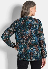 Blusa a maniche lunghe in un motivo astratto nei toni del verde scuro, blu e marrone, con scollatura arricciata e polsini leggermente elasticizzati.