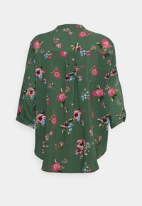 Blusa verde floreale con maniche a tre quarti, caratterizzata da fiori rosa, rossi e blu. Vestibilità ampia con un dettaglio a piega sul retro. Tessuto morbido.
