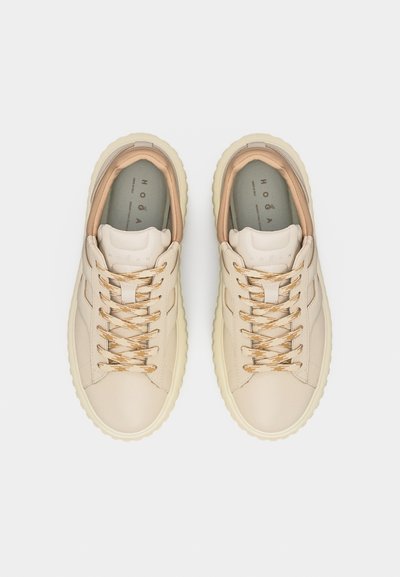 Ζεύγος μπεζ δερμάτινα sneakers με χοντρές σόλες και κορδόνια με σχέδιο, φωτογραφημένα από ψηλά πάνω σε λευκό φόντο.