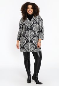 Zwart-witte tuniek met een palmenbladpatroon, gecombineerd met glanzende zwarte leggings en hoge laarzen, met 3/4 mouwen en een v-hals.