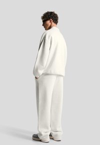 Bela flis pulover in ustrezne hlače, sproščenega kroja, z žepi in teksturirano tkanino. Črne športne čevlje dopolnjujejo obleko.
