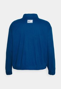 Giacca in pile blu Nike con colletto alto, polsini a coste e orlo inferiore. Presenta un'etichetta con il logo nella zona del collo. Texture morbida.