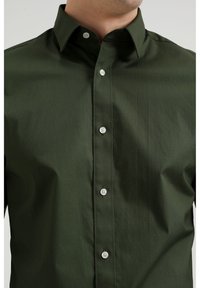 Mörkgrön skjorta med knappar i slätt, rynkbeständigt tyg. Har en klassisk krage, vita knappar och en skräddarsydd passform.