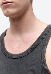 Záber zblízka na krk a hornú časť hrudníka osoby nosiacej tmavosivý rebrovaný tielko, s viditeľnou pokožkou a ochlpením na hrudi.