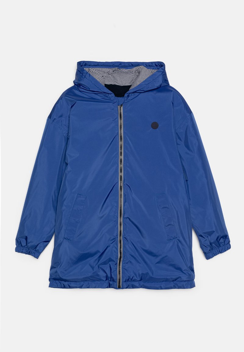 Giacca impermeabile blu con cappuccio, caratterizzata da un accento circolare nero, polsini elasticizzati e foderatura interna a righe. Chiusura frontale con zip e tasche laterali.