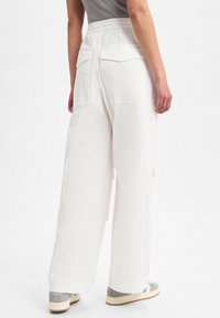 Vloeiende witte broek met een brede pijp, elastische tailleband en twee achterzakken. De stof lijkt zacht met een gladde textuur.