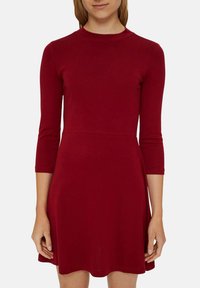 Czerwona sukienka z długim rękawem, wykonana z elastycznego materiału, z okrągłym dekoltem i rozkloszowanym dołem, który kończy się powyżej kolan. Gładka faktura.