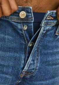 Tmavě modré džíny z denimu s klasickým designem, s stříbrným kováním, kontrastním oranžovým šitím a zapínáním na horní knoflík.