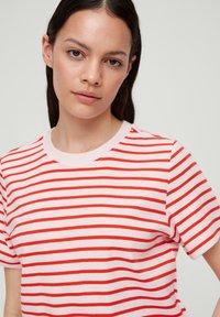 Rood-wit gestreept T-shirt van zacht katoen. Heeft een ronde hals en korte mouwen; de strepen wisselen van dikte over de stof.